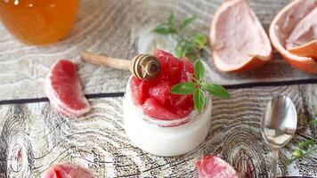 homemade sweet yogurt in a glass jar with pieces of red ripe grapefruit and honey, on a wooden table video