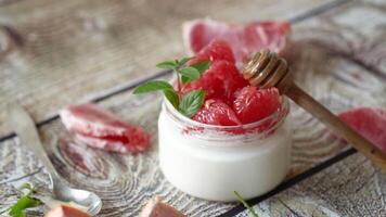 homemade sweet yogurt in a glass jar with pieces of red ripe grapefruit and honey, on a wooden table video