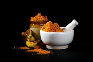 Turmeric powder in mortar and mortar on black background photo