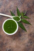 Green paste in a bowl with a spoon on a brown background photo