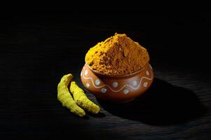 Turmeric powder in clay pot with roots or barks on black background photo