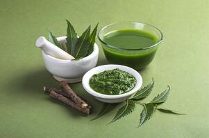 Medicinal Neem leaves in mortar and pestle with neem paste, juice and twigs on green background photo