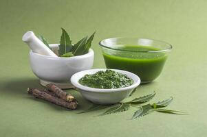 Medicinal Neem leaves in mortar and pestle with neem paste, juice and twigs on green background photo