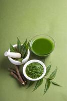 Medicinal Neem leaves in mortar and pestle with neem paste, juice and twigs on green background photo