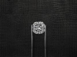 Cut Beautiful diamond held by tweezers, on a black leather background photo