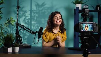 Happy online show host hitting the record button on professional camera, using microphone to talk about today topic with subscribers. Cheerful influencer filming creative vlog video