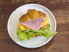 Croissants with stuffing in a plate on a wooden dining table. croissant with chicken sausage, ham, omelet and vegetables,tomato . The concept of breakfast, fast food, snack. photo