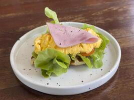Croissants with stuffing in a plate on a wooden dining table. croissant with chicken sausage, ham, omelet and vegetables,tomato . The concept of breakfast, fast food, snack. photo