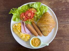 Croissants with stuffing in a plate on a wooden dining table. croissant with chicken sausage, ham, omelet and vegetables,tomato . The concept of breakfast, fast food, snack. topview photo