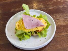 Croissants waffle with stuffing in a plate on a wooden dining table. croissant waffle with chicken sausage, ham, omelet and vegetables,tomato . The concept of breakfast, fast food, snack. photo