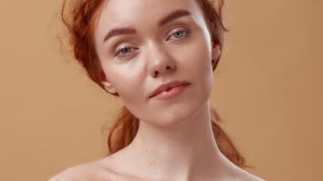 A young woman with soft, light red hair gazes directly at the viewer. She stands in front of a warm-toned background, exuding a calm and inviting presence. video