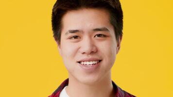 A young Asian guy with short black hair passionately expresses thoughts while standing in front of a bright yellow background, creating an engaging atmosphere filled with energy. video