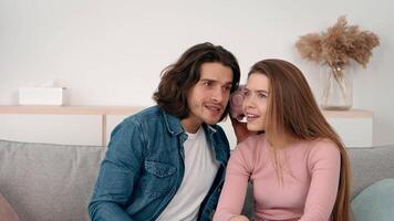 A young couple enjoys a lighthearted conversation while sitting close together on a comfortable sofa. Natural light fills the room, creating a warm and inviting atmosphere. video