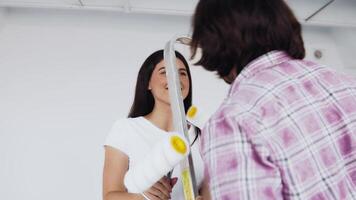 Two people are joyfully getting ready to paint a room, holding paint rollers and interacting with enthusiasm. The bright interior enhances the cheerful atmosphere of their activity. video