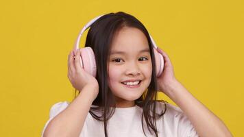 Asian girl enjoys music with headphones on, beaming with happiness in front of a vibrant yellow backdrop. video