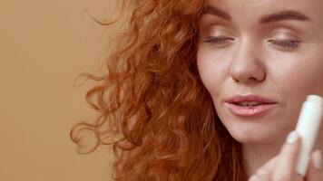 A young woman with vibrant curly red hair gazes softly, displaying a warm smile. The backdrop is a soothing orange hue, creating a relaxed and inviting atmosphere. video