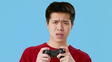 A young Asian man holds a gaming controller with concentration on his face. He appears to be deeply engaged in his game, highlighting the passion for gaming and virtual entertainment. video