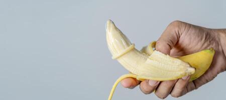 A man shows how to put a condom on his penis using a banana demonstration. Studio shot on gray background, panoramic image. photo