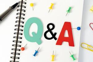 Blank multi-colored note paper with QA or questions and answers written on it. Top view of pen and glasses writing Q and A on desk. photo