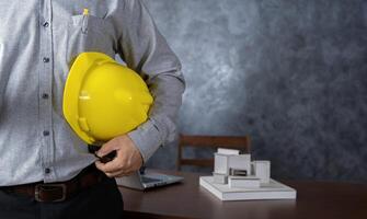 Close-up of Engineer holding helmet checking accuracy of building structural blueprints from architect on the desk in office to proceed with the construction. photo