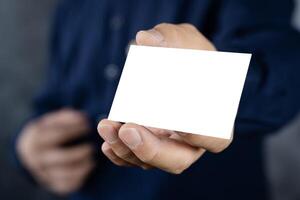 Man holding white business card on concrete wall background, adult man hand holding empty business card in front of camera. photo