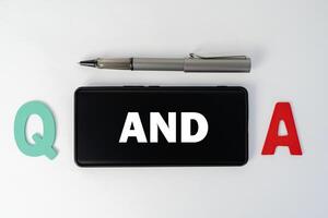 Q and A word on a smartphone and pen, white work desk background. Questions and answer concept. photo