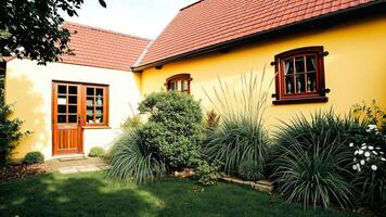 yellow house with a red roof amidst lush greenery photo