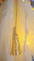 golden tassel hanging from a white string-like object with blurred yellow lights photo