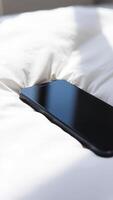 black smartphone rests on a white bedspread photo