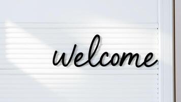 black cursive welcome sign on a white slatted surface photo