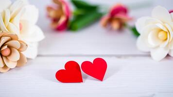 two red paper hearts rest on a white wooden surface surrounded by delicate paper flowers photo