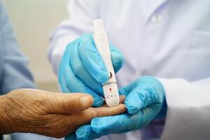 Asian doctor using digital glucose meter for check sample blood sugar level to treatment diabetes. photo