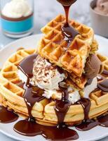 A waffle with ice cream and chocolate syrup being poured on top photo