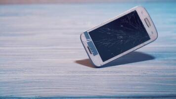 Modern white touchscreen phone is falling on the floor and crashes isolated on the wooden background floor. Broken smartphone on the grey surface. video