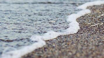 Surface of water sea ocean wave with white foam close-up on a beach. Beautiful waves of water crashing onto the small rocks and shore. Summer vacation holiday at the sea. video
