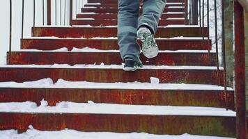 A worker in gray pants with a light horizontal stripe and black boots is climbing up steps in the street in the winter. Close-up of legs. View of back. video