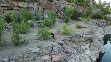Young tourist man standing on steep slope with backpack over the water. Camper observing beautiful view of canyon with green trees and bushes and their reflection in the water. Aerial view video