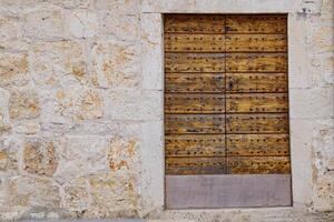 This image showcases a rustic wooden door, showcasing deep grooves and a weathered finish, framed by an aged stone wall with various shades and textures, evoking a sense of history and charm. photo