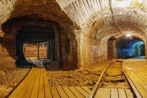 Venture into the depths of an old abandoned mine tunnel, where shadows dance along the wooden walkway and rusty tracks evoke a sense of mystery and exploration in this long-forgotten place. photo