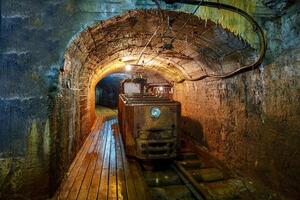 Old rusty mining train in a dark tunnel under the mountain. The tunnel is illuminated by a few light bulbs, with wooden tracks and walls made of carved rocks in an abandoned silver mine. photo