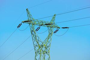 A green electricity pylon rises against a clear blue sky, symbolizing modern energy infrastructure. Its lattice design showcases engineering advancements for efficient power transmission. photo
