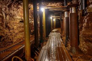 Explore the hidden wonders beneath the earth with this image of an industrial walkway leading into an underground mine tunnel, where wooden planks guide you through rocky walls. photo
