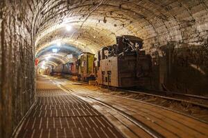 A rusty old mining train sits in a dark, eerie mine tunnel. The wooden tracks are covered in dust, and the atmosphere is tense, evoking a sense of abandonment and mystery. photo