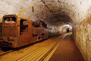 An old rusty mining train sits abandoned in a dark tunnel. The tracks lead into the shadows, creating a mysterious atmosphere, ideal for stories about mining and industry. photo