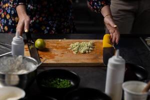Hands of woman chopping fresh avocado on wooden board, with lime beside it. Various ingredients are ready for preparation photo