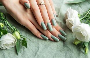 Elegant hands adorned with green nail polish surrounded by white roses and greenery on a soft fabric background during daylight photo
