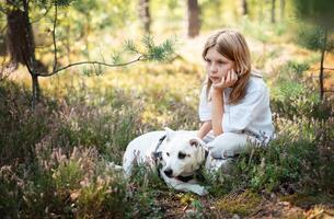 A child relaxing with a dog in a serene forest, surrounded by greenery and blooming flowers on a sunny day photo