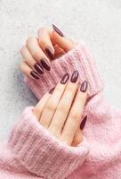 Elegant maroon manicured nails displayed against a soft pink sweater on a textured gray background photo