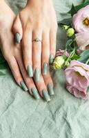 Elegant hands with green nail polish resting on a soft fabric surrounded by delicate flowers in a tranquil setting photo