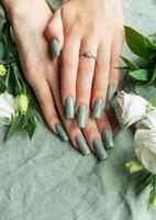 Elegant hands adorned with green nail polish surrounded by white roses and greenery on a soft fabric background during daylight photo